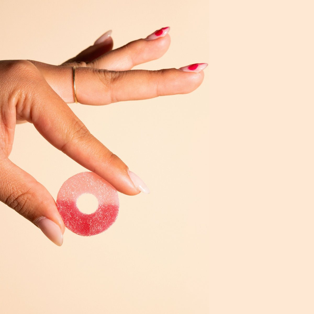 Hand holding a pink gummy candy against a beige background